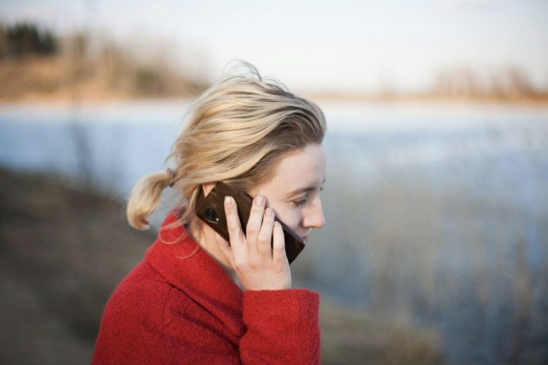 A woman in a red coat talking on a phone by a tranquil lake, exemplifying the ease of identifying service providers using Free Carrier Lookup for strategic telecommunication planning.